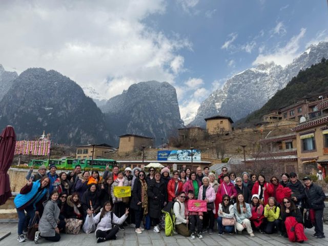 Super Travels tour group at a Tibetan village beneath snow-capped peaks, Yunnan